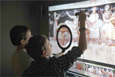 Figure 1: Two young visitors exploring multiple layers of information in the electronic reproduction of a wall painting with Polyapton. Besides a finger touch, the system is sensitive to the touch of particular objects with different functionalities.